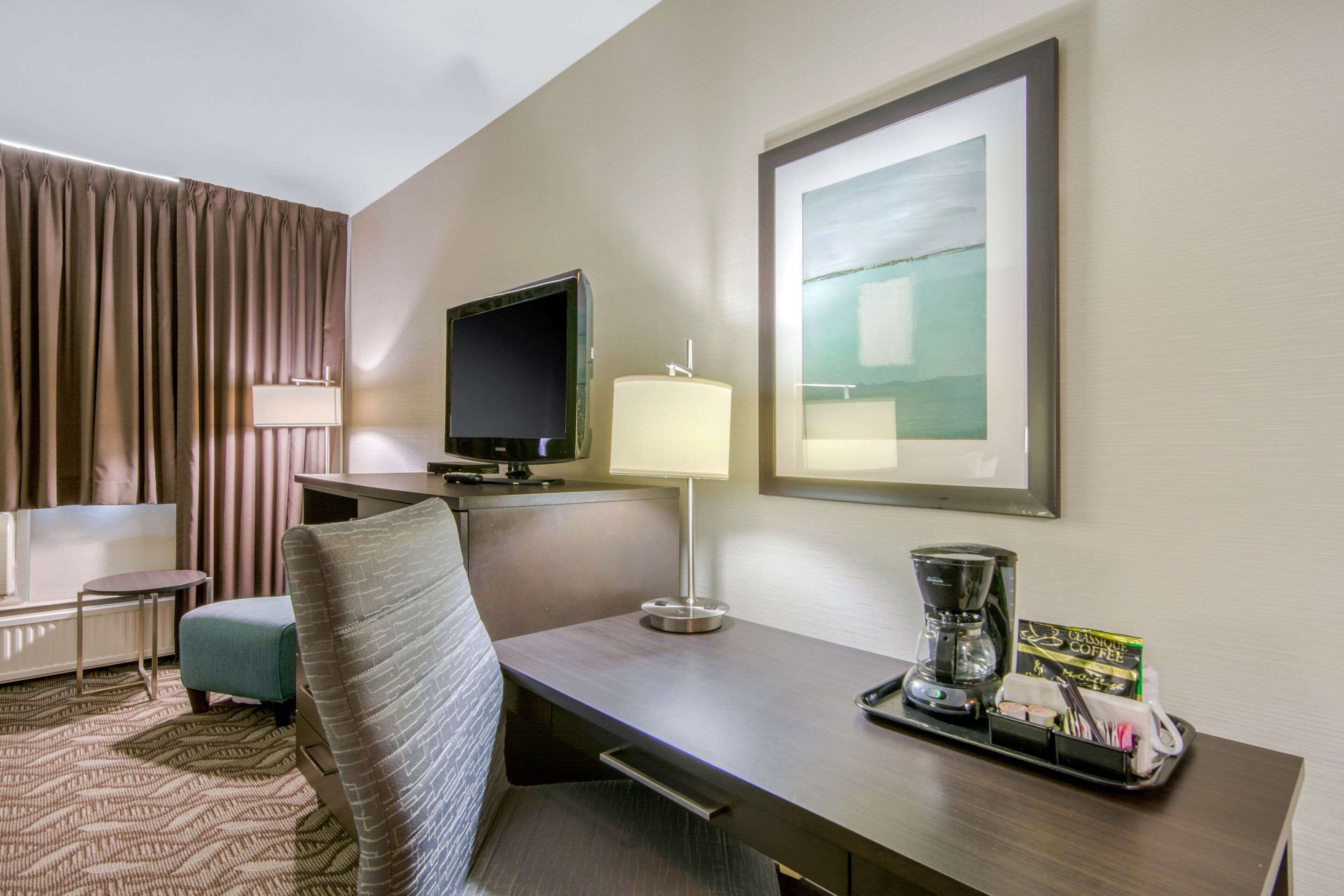 A hotel room with a bed, a desk with a lamp, a television, and a coffee maker.