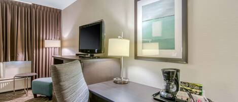 A hotel room with a bed, a desk with a lamp, a television, and a coffee maker.