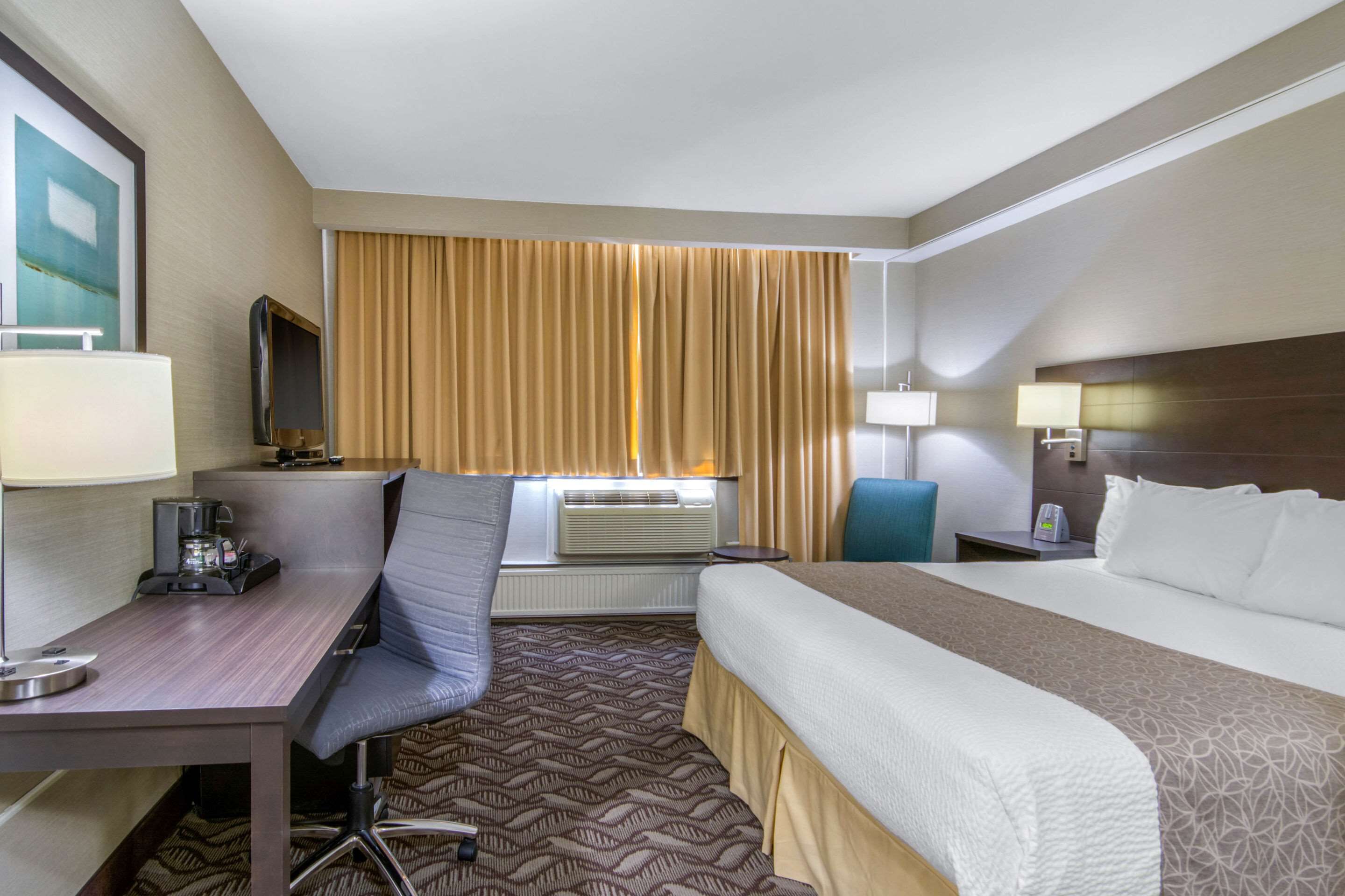 A hotel room with a bed, desk, chair, and a television.