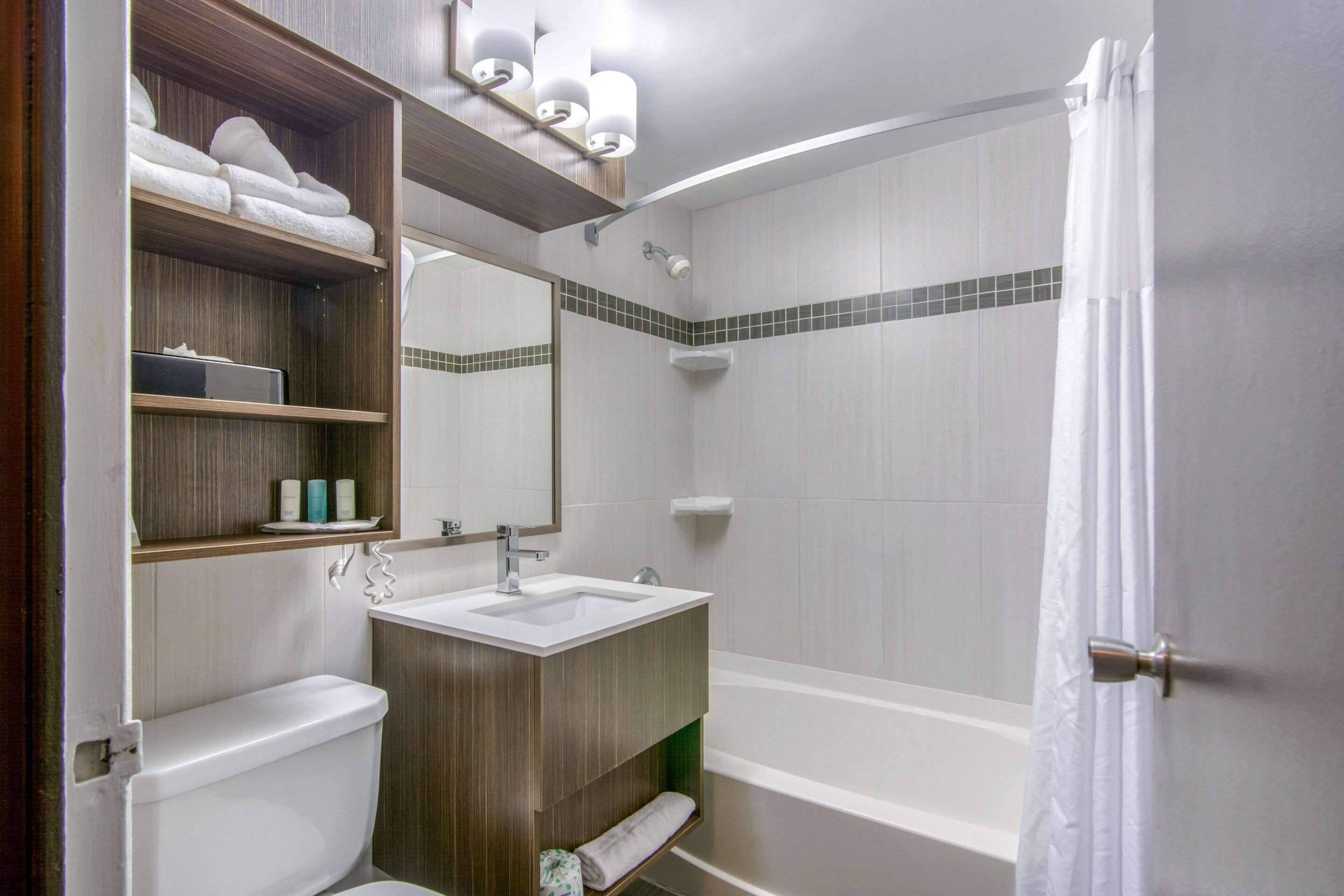 A modern bathroom with a toilet, sink, and bathtub. There are shelves with towels and toiletries.