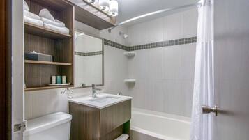 Une salle de bain moderne équipée de toilettes, d’un lavabo et d’une baignoire. On y trouve des étagères avec des serviettes et des articles de toilette.