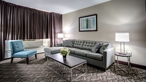 Une chambre d’hôtel moderne avec un canapé gris, un fauteuil bleu, une table basse et une table d’appoint avec une lampe.