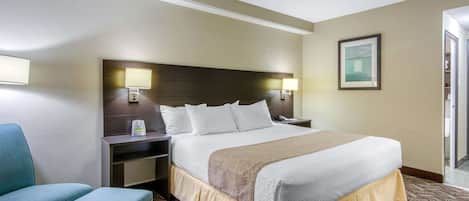 Ein Hotelzimmer mit einem großen Bett, einem Nachttisch mit Lampe, einem Sessel und einem gerahmten Bild an der Wand.