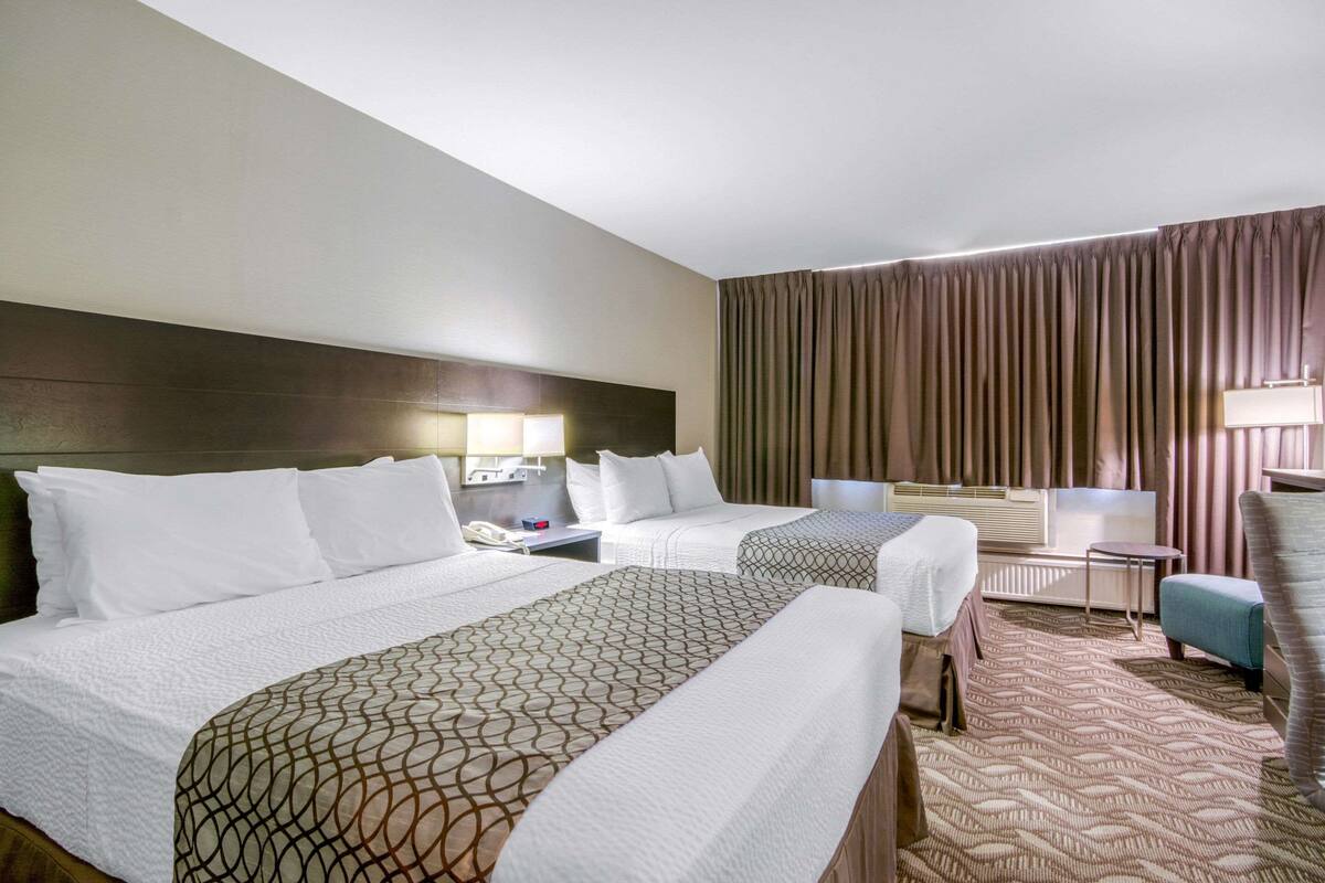 Ein Hotelzimmer mit zwei Betten, einem Schreibtisch, einem Stuhl und einem großen Fenster mit Vorhängen.