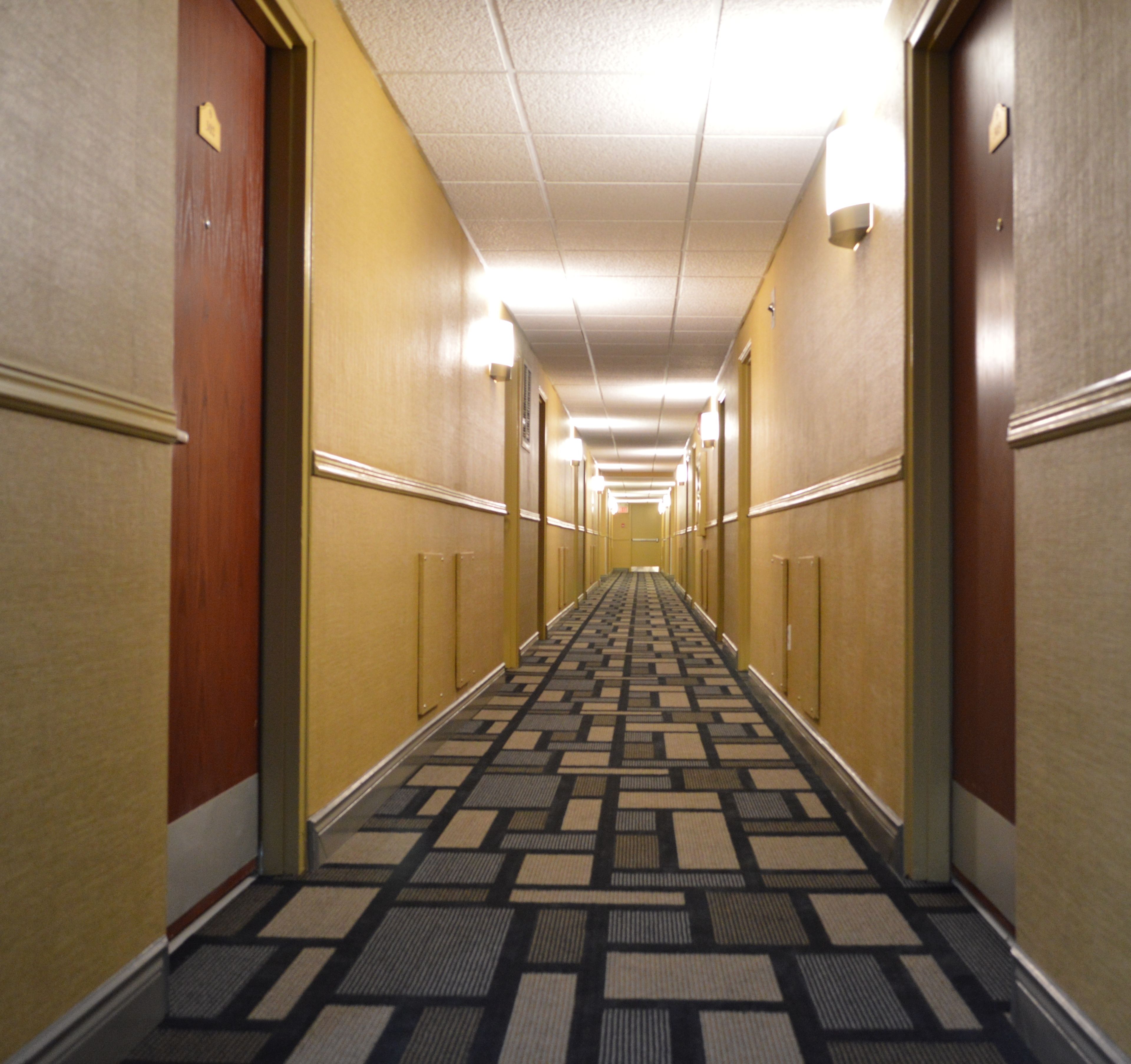 Un couloir d’hôtel avec un tapis à motifs, des murs jaunes et des portes de chaque côté.