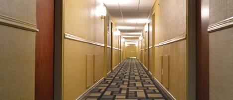 Pasillo de hotel con alfombra estampada, paredes amarillas y puertas a ambos lados.