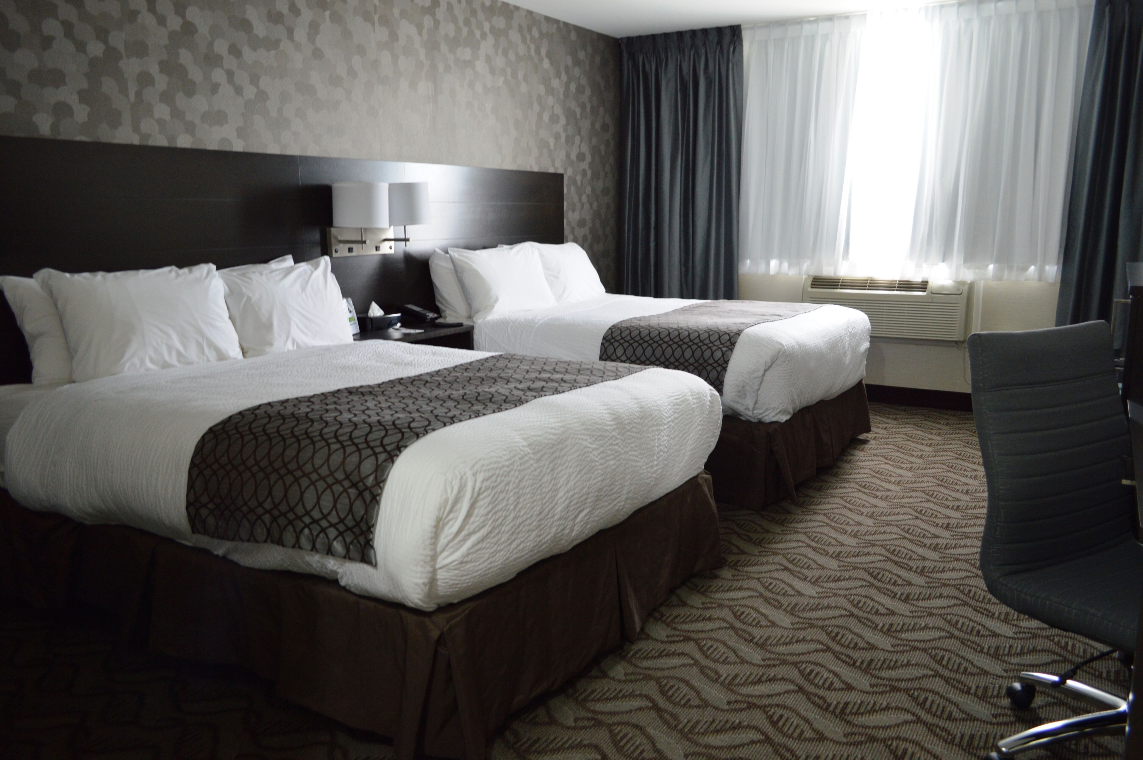 A hotel room with two beds, a desk, a chair, and a window with curtains.