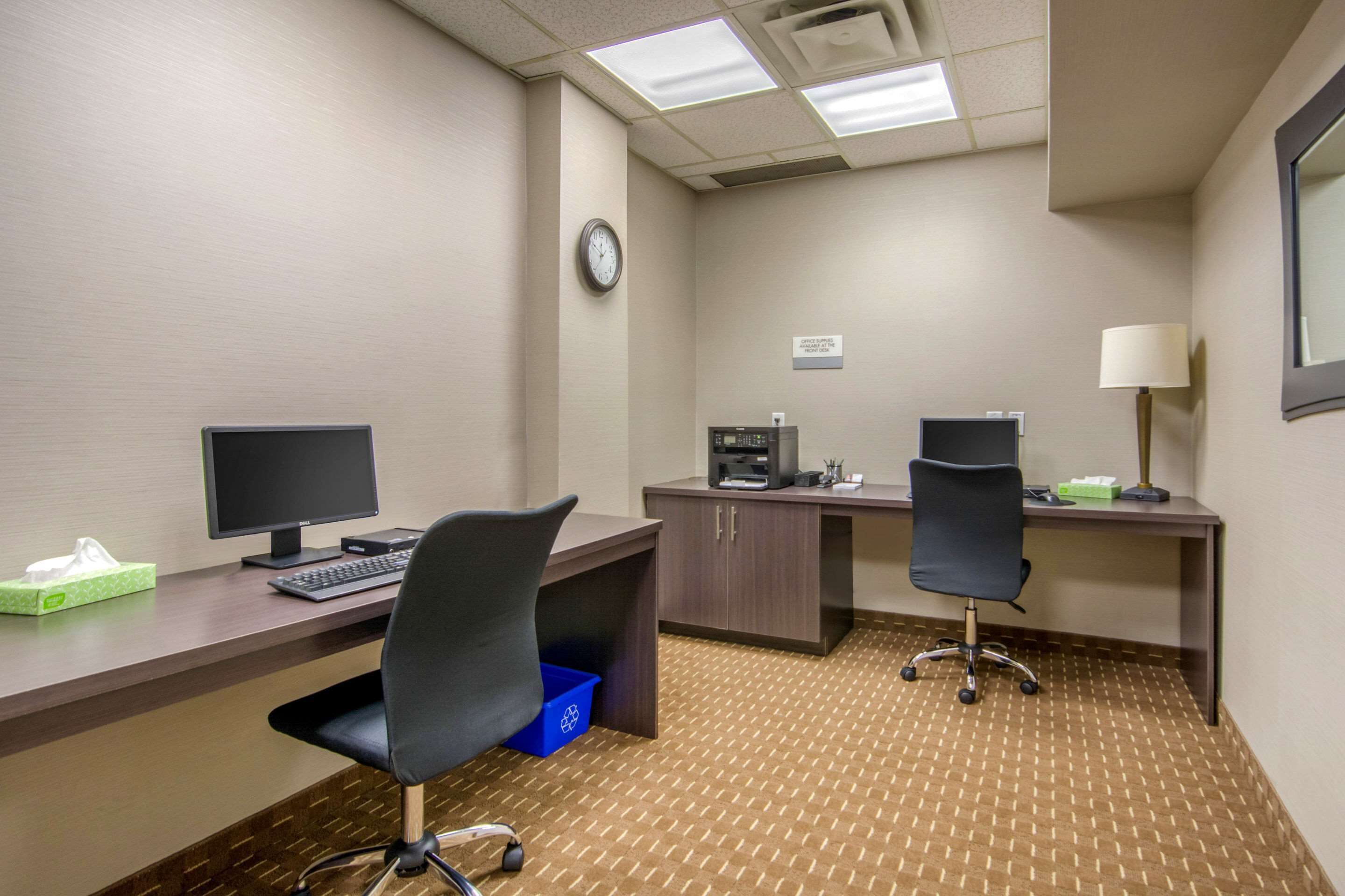A hotel office with two desks, computers, chairs, a clock, and a trash bin.