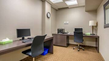 A hotel office with two desks, computers, chairs, a clock, and a trash bin.