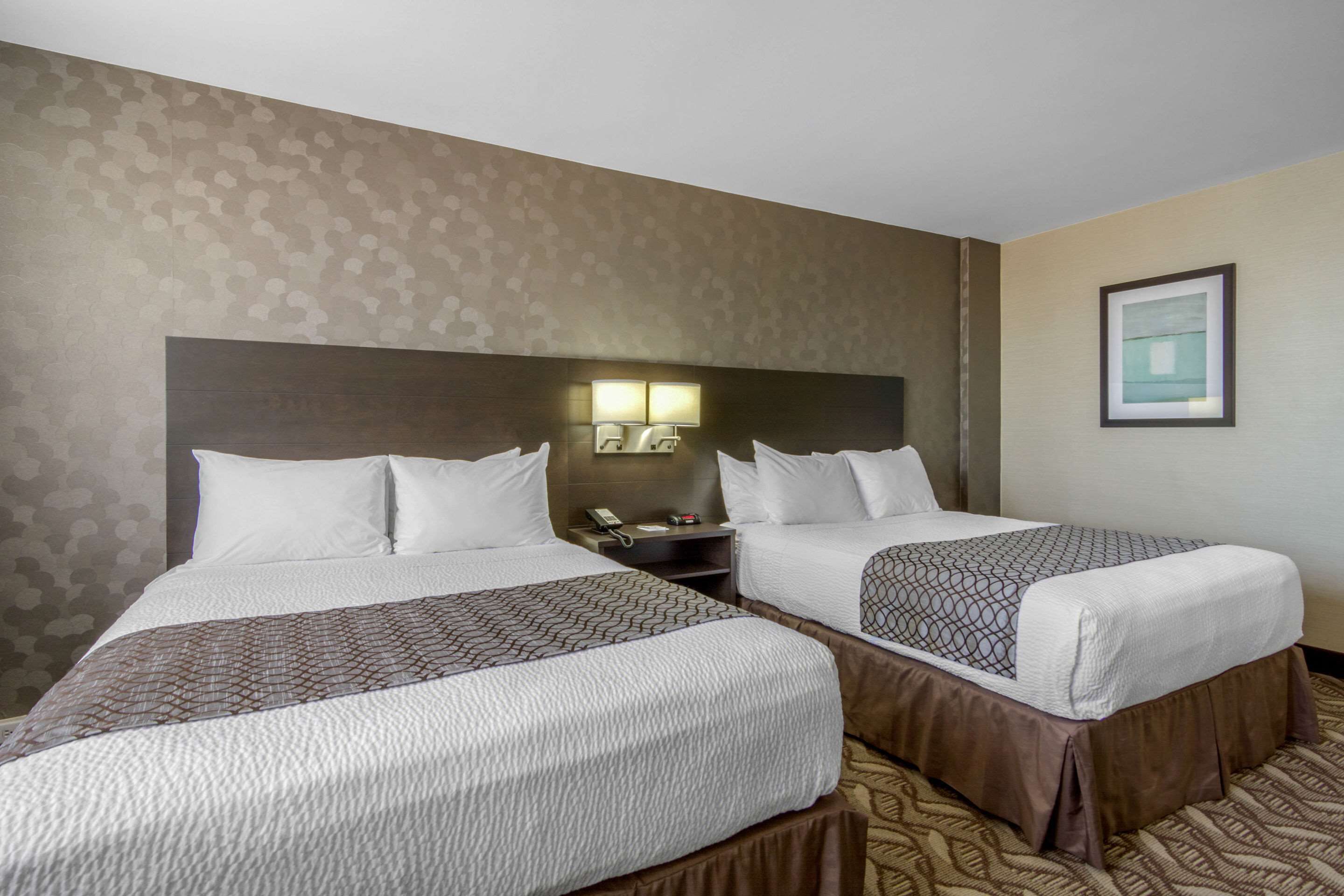 A hotel room with two beds, a nightstand with a lamp, and a framed picture on the wall.