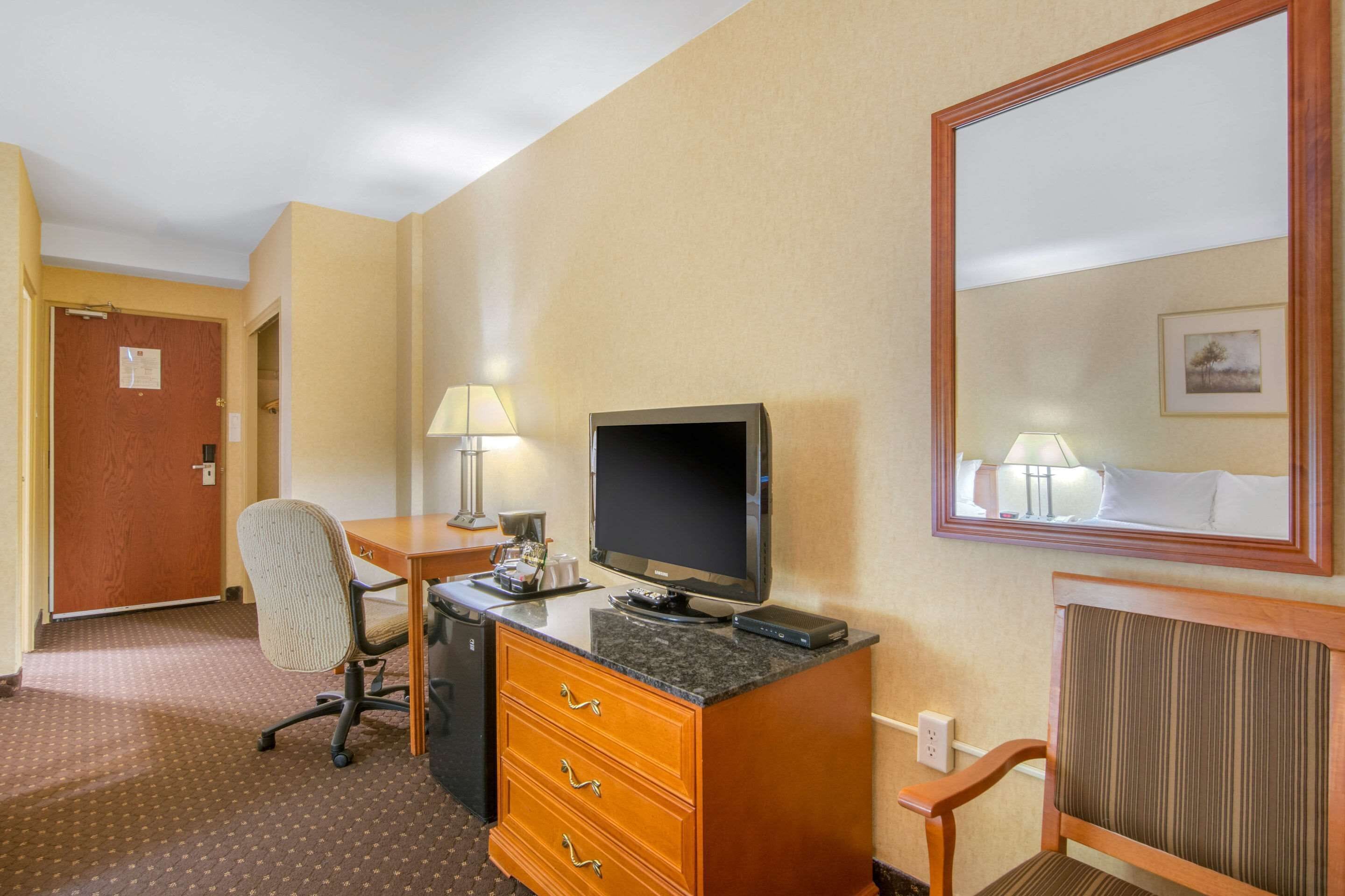 A hotel room with a desk, chair, television, and a mirror.