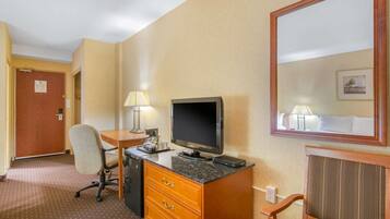 A hotel room with a desk, chair, television, and a mirror.