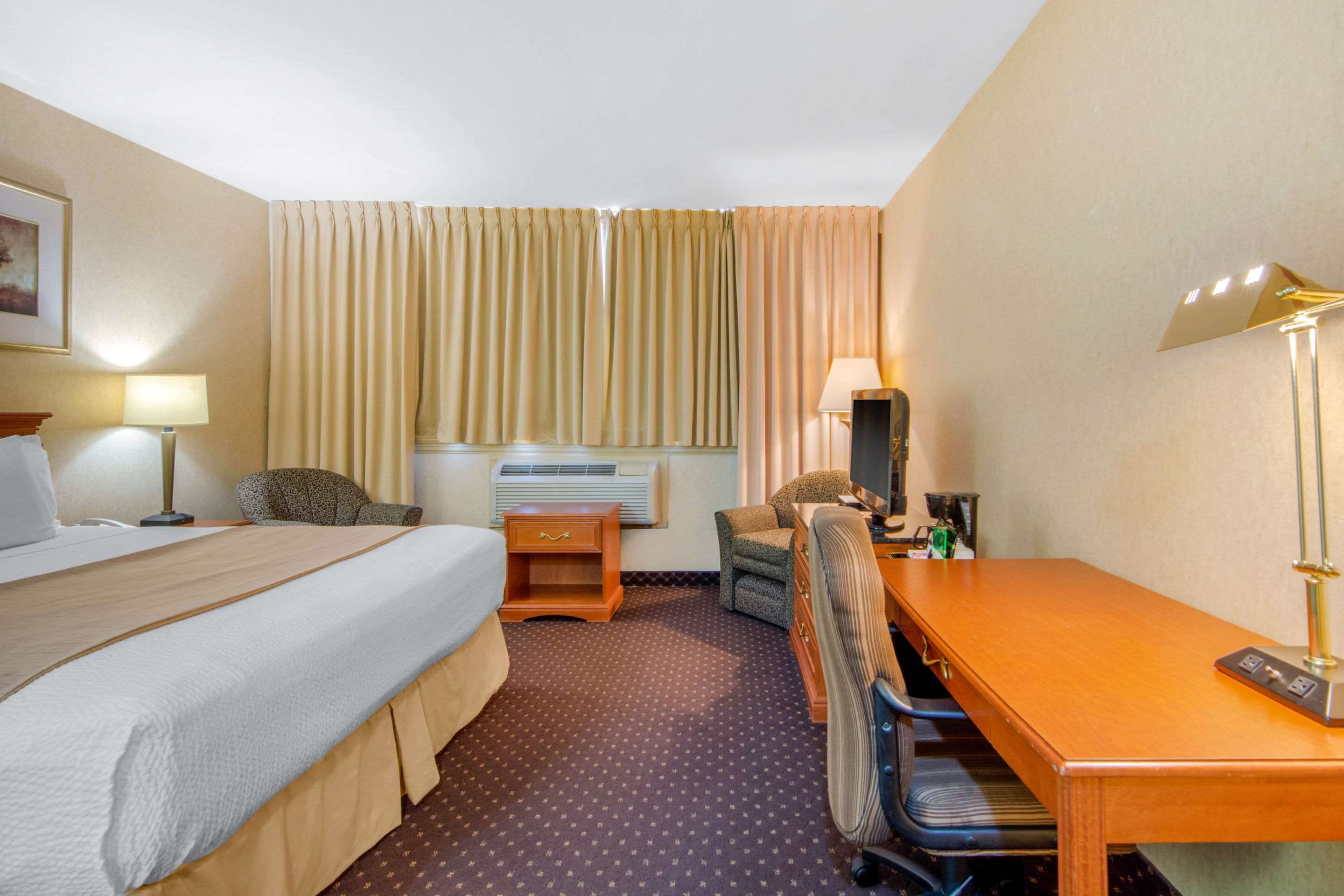 A hotel room with a bed, a desk, a chair, a lamp, and a window with curtains.