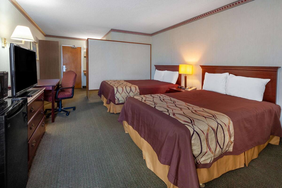 Una habitación de hotel con dos camas, un escritorio con televisor, una silla y una lámpara de escritorio.