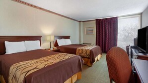 Quarto de hotel com duas camas, uma escrivaninha, uma cadeira, uma televisão e uma janela com cortinas.