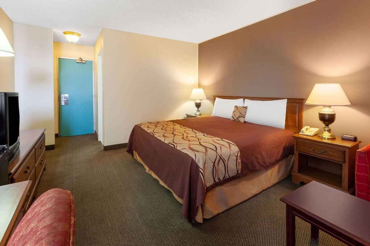 Una habitación de hotel con cama, lámparas de noche, un escritorio, una silla y un televisor.
