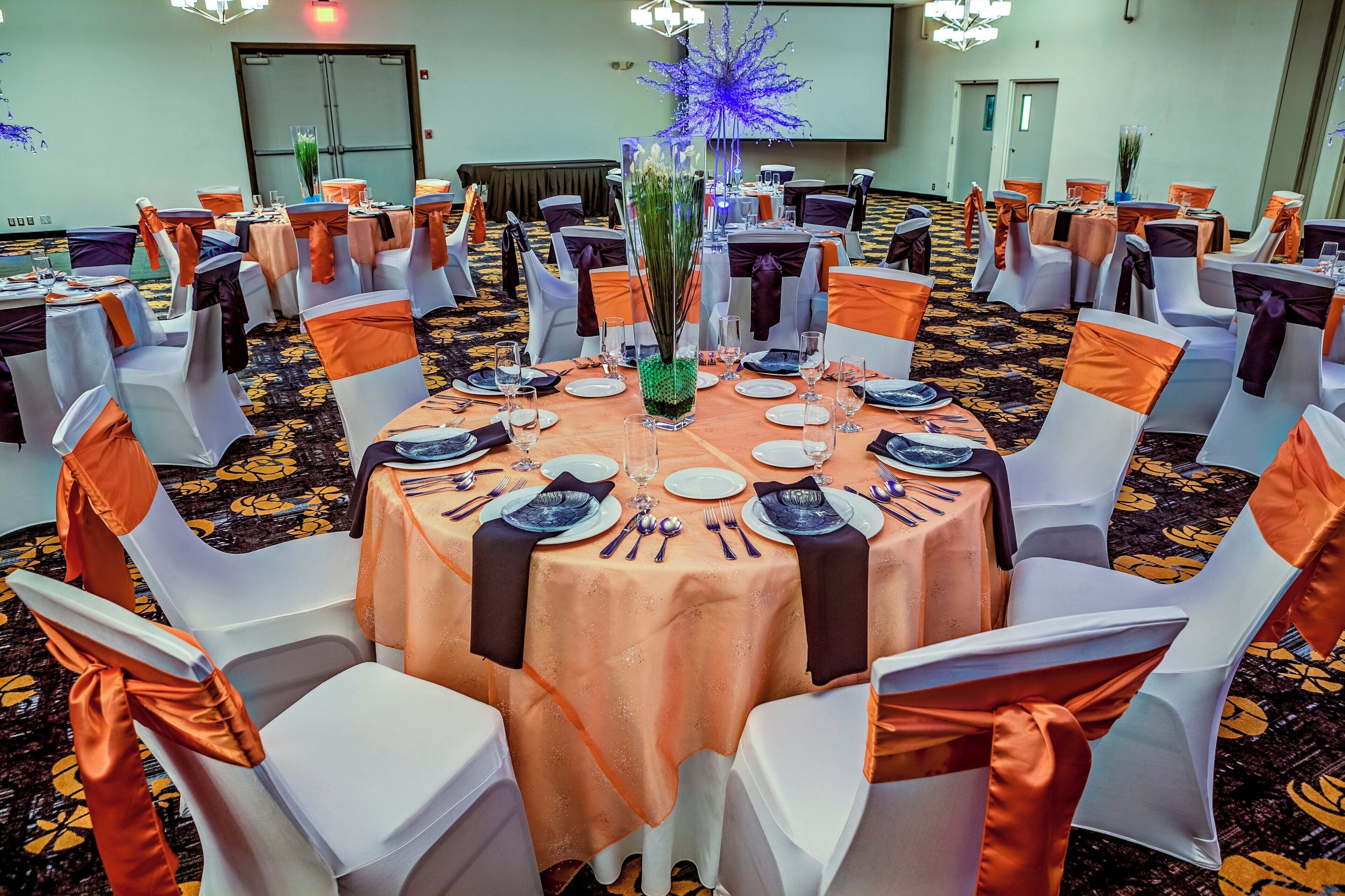 Uma sala de banquetes com mesas redondas, cadeiras brancas e fitas laranja.