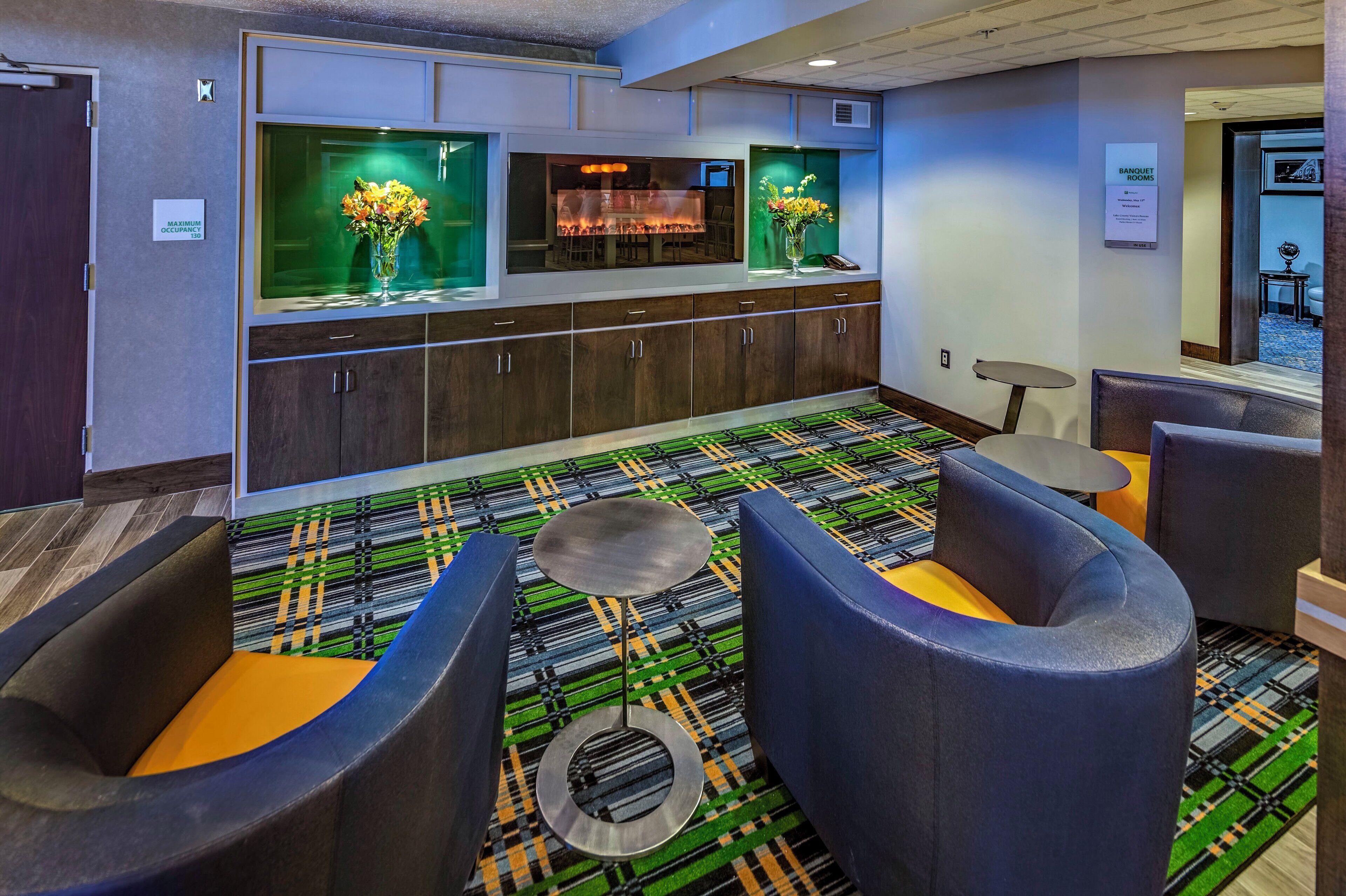 A hotel lobby with a bar area, seating with a patterned carpet, and a sign indicating the maximum occupancy.