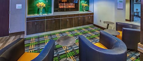 A hotel lobby with a bar area, seating with a patterned carpet, and a sign indicating the maximum occupancy.