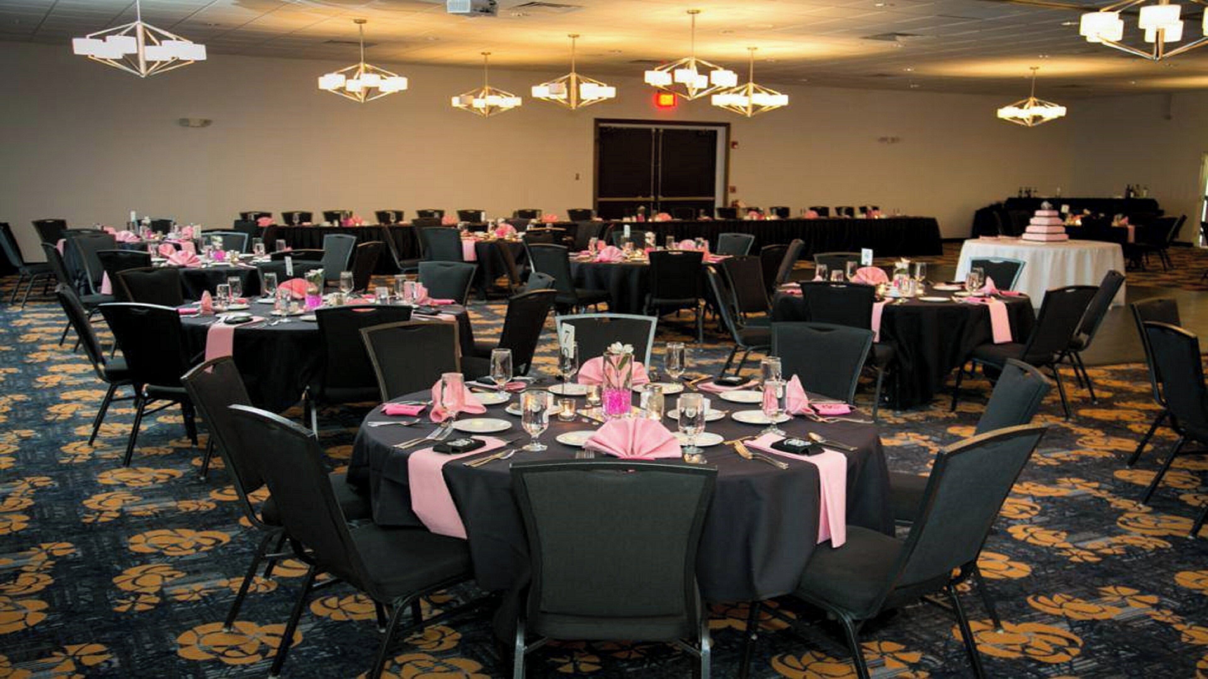 Uma sala de banquetes com mesas redondas, cadeiras pretas e toalhas de mesa cor-de-rosa.