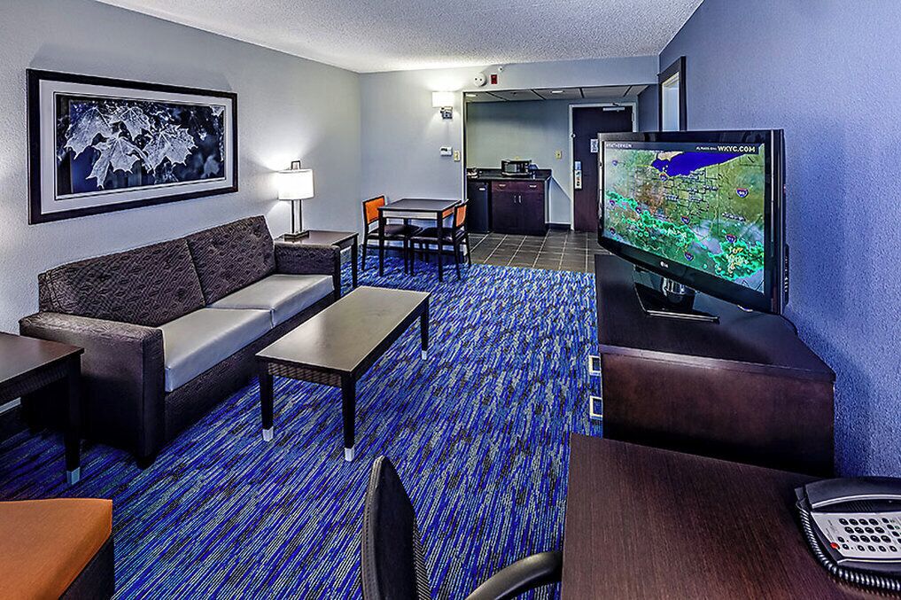 Quarto de hotel com sofá, mesa pequena, televisão e secretária com telefone.