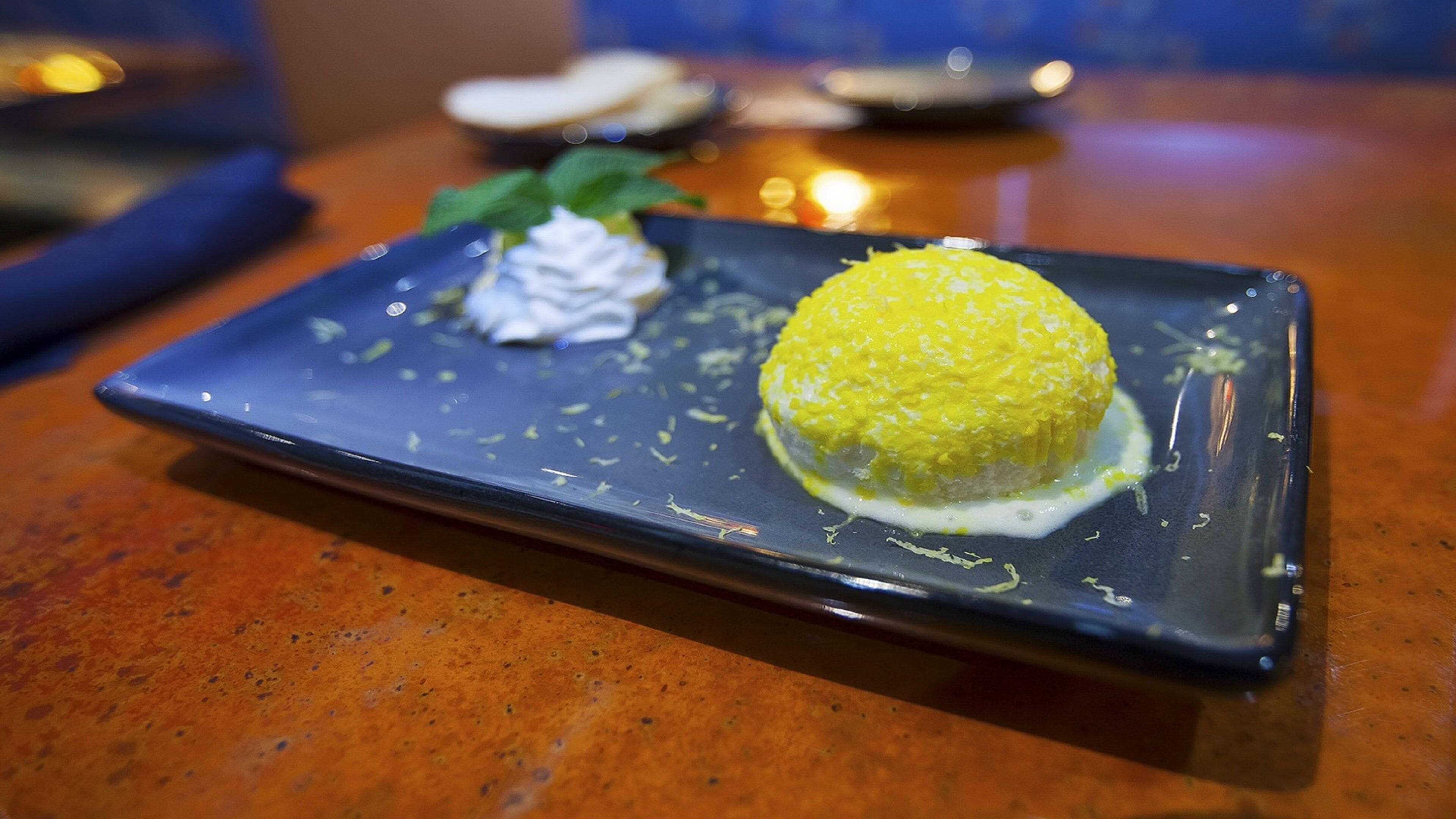 Un postre sobre un plato rectangular con salsa cremosa y una guarnición en una encimera veteada.