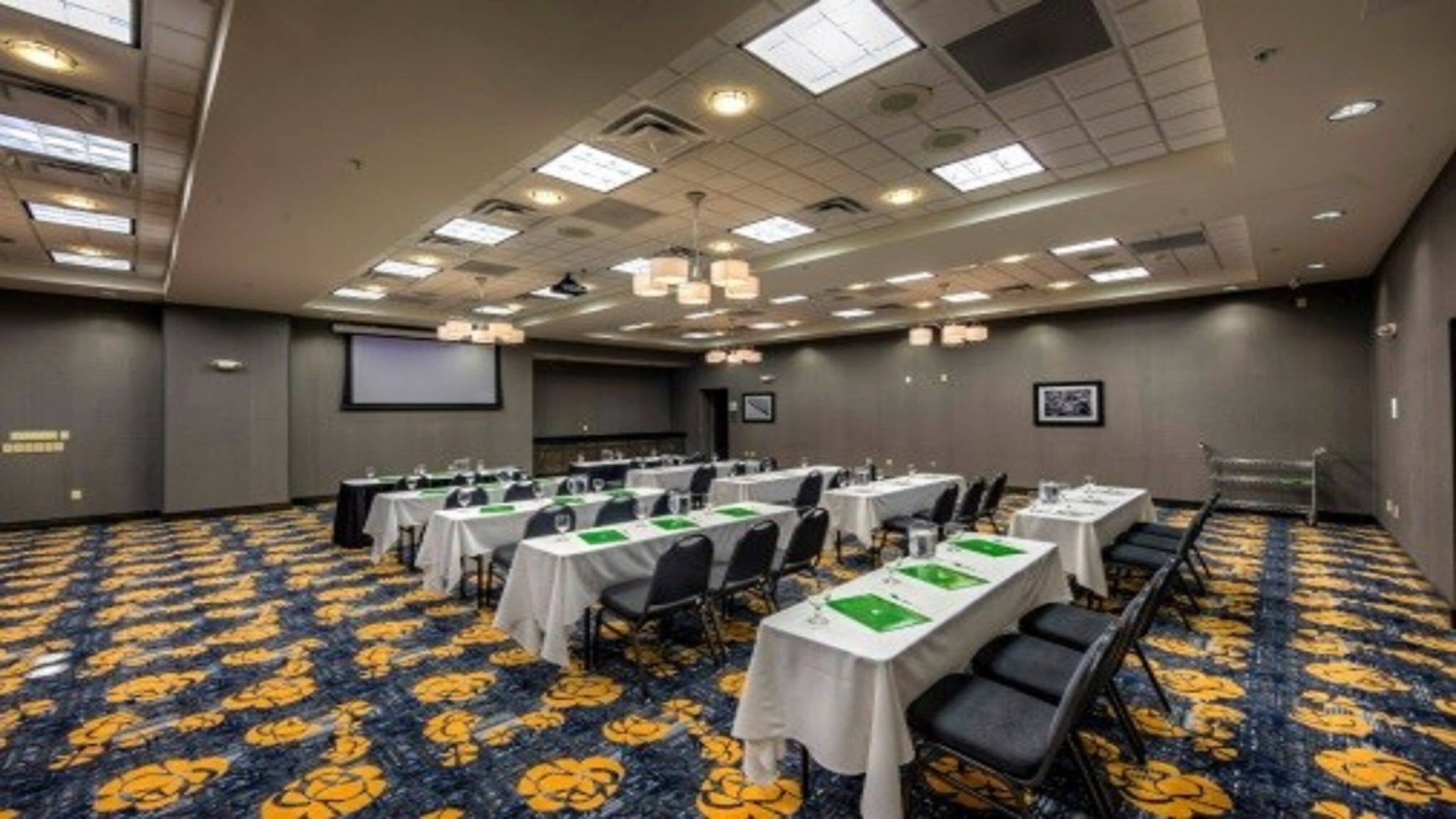 A conference room with multiple tables, chairs, and a projector screen.