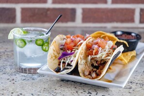 Two tacos on a white plate with a side of salsa and a glass of iced drink with lime slices. - Holiday Inn Cleveland Northeast - Mentor by IHG (Mentor)