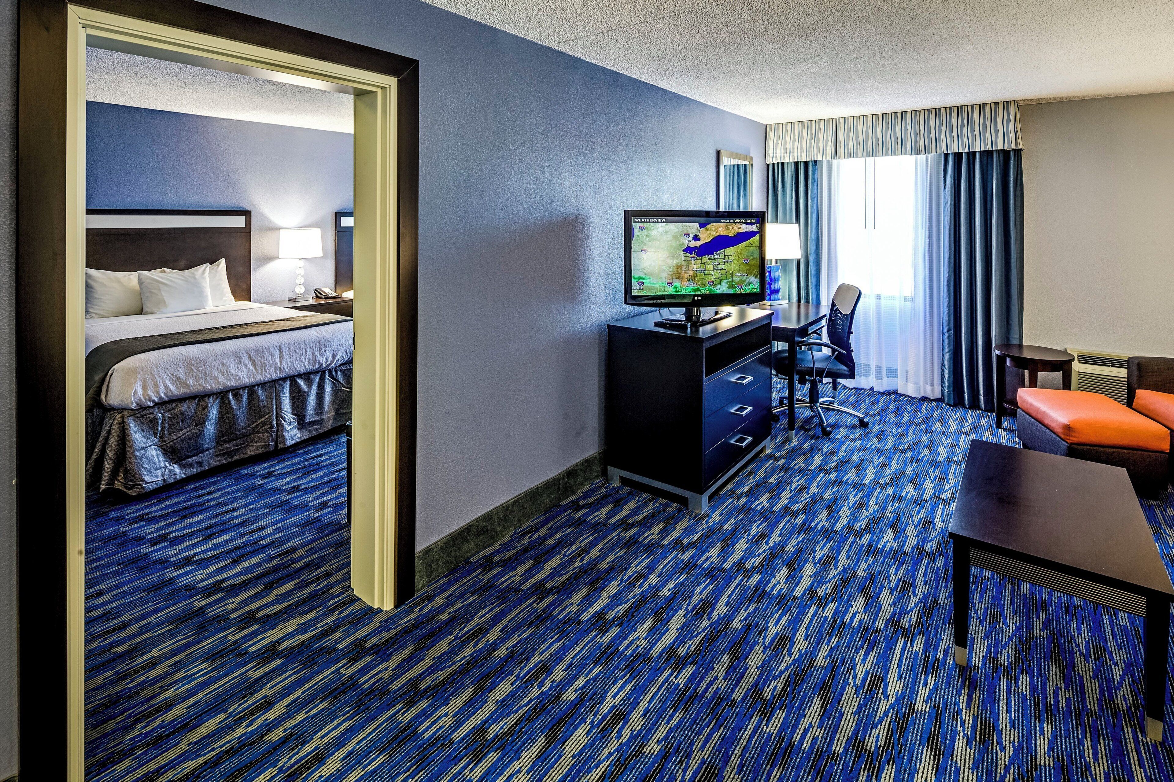 A hotel room with a bed, a desk, a television, and a seating area.