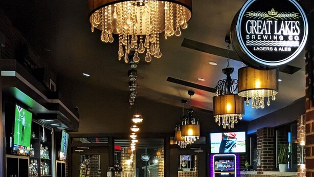 Un espace bar offrant différentes options de sièges, un comptoir avec une caisse enregistreuse et un panneau néon représentant la brasserie Great Lakes Brewing Co.