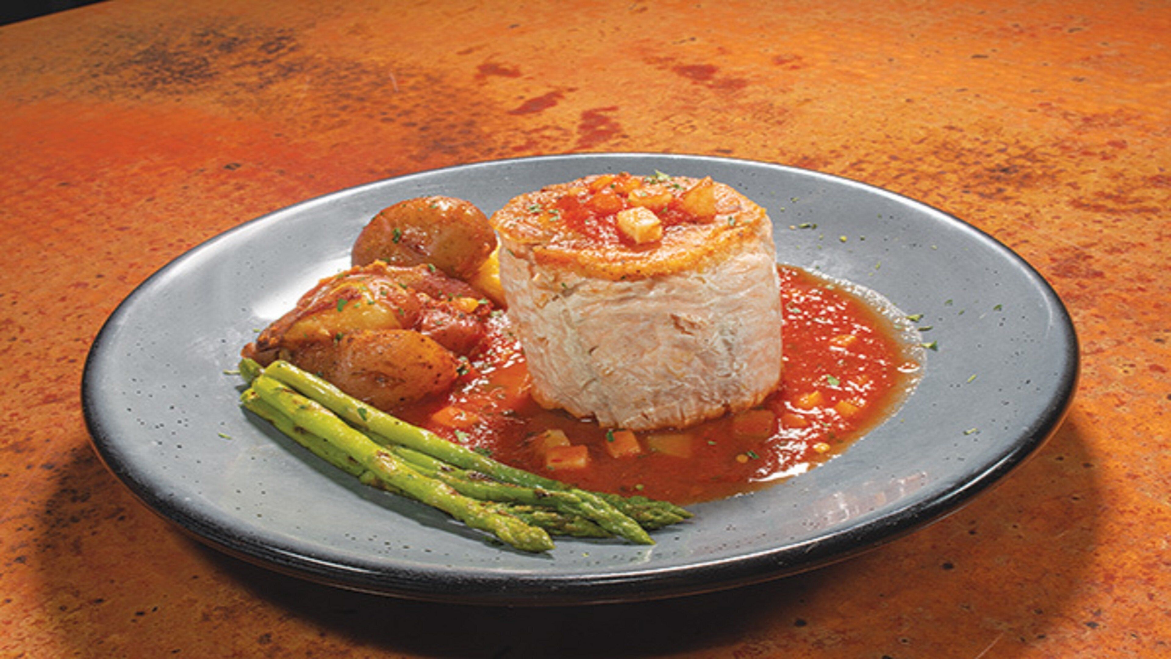A plate with a rolled pastry, asparagus, and a tomato-based sauce.