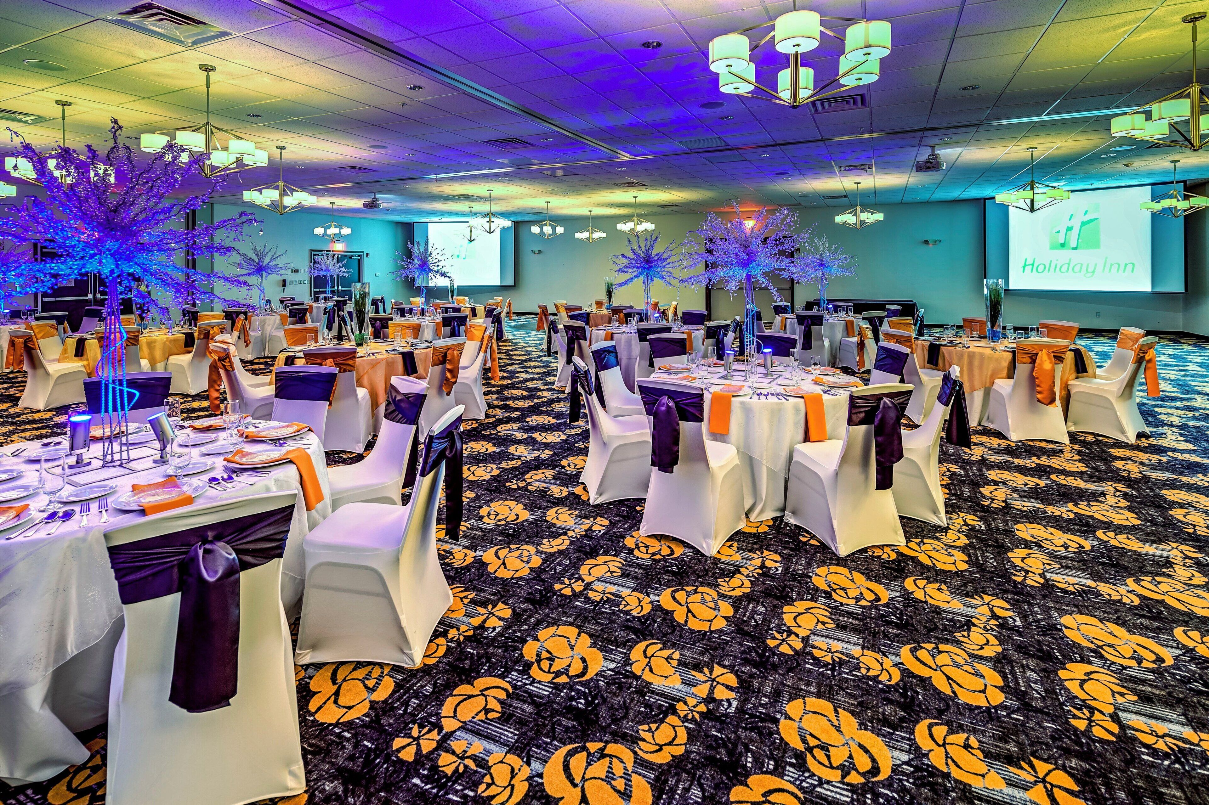 Une salle de banquet avec des tables rondes, des chaises blanches et un tapis orné de motifs floraux.