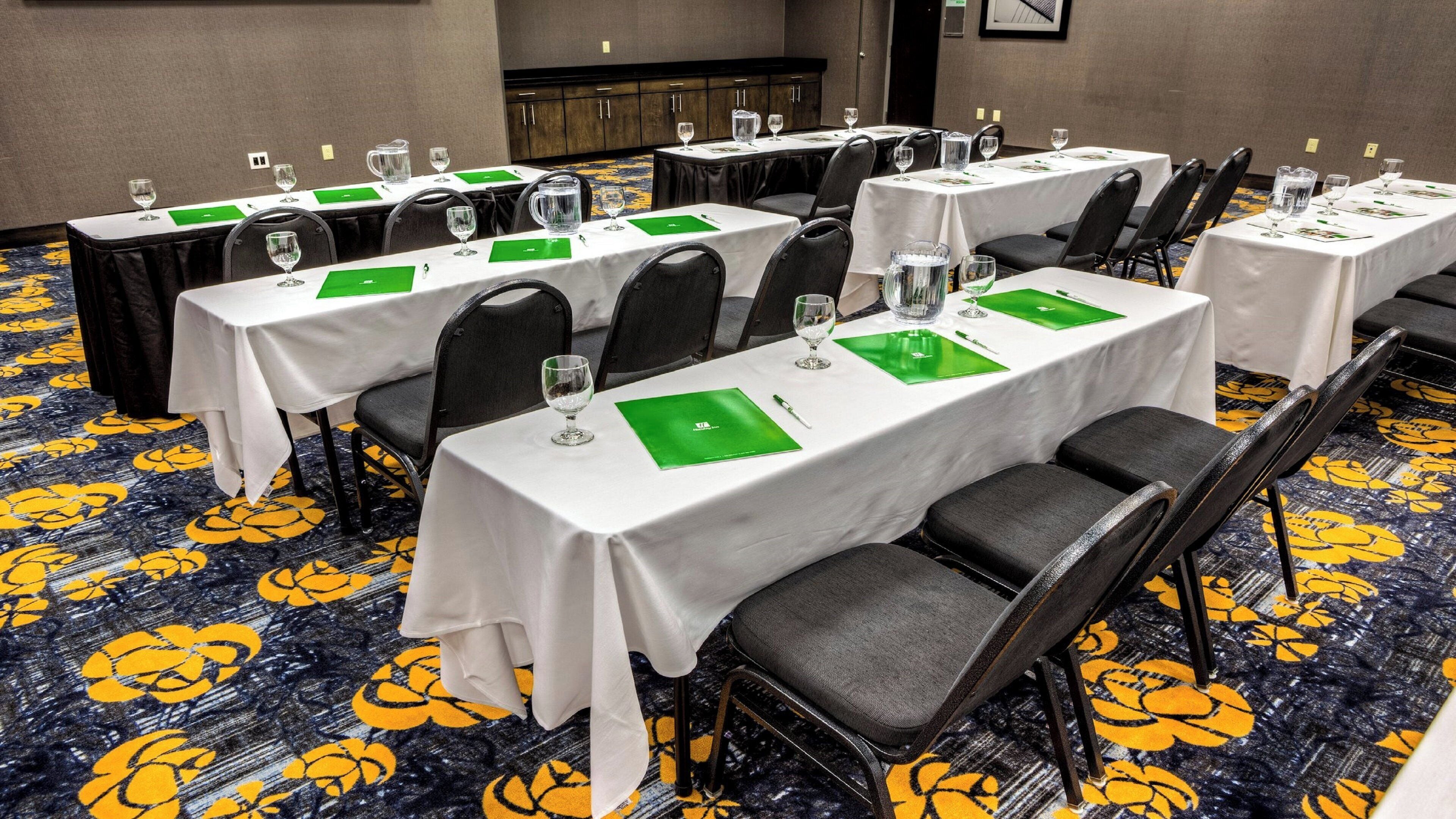 A conference room with multiple tables, each with chairs, glasses, and green placemats.