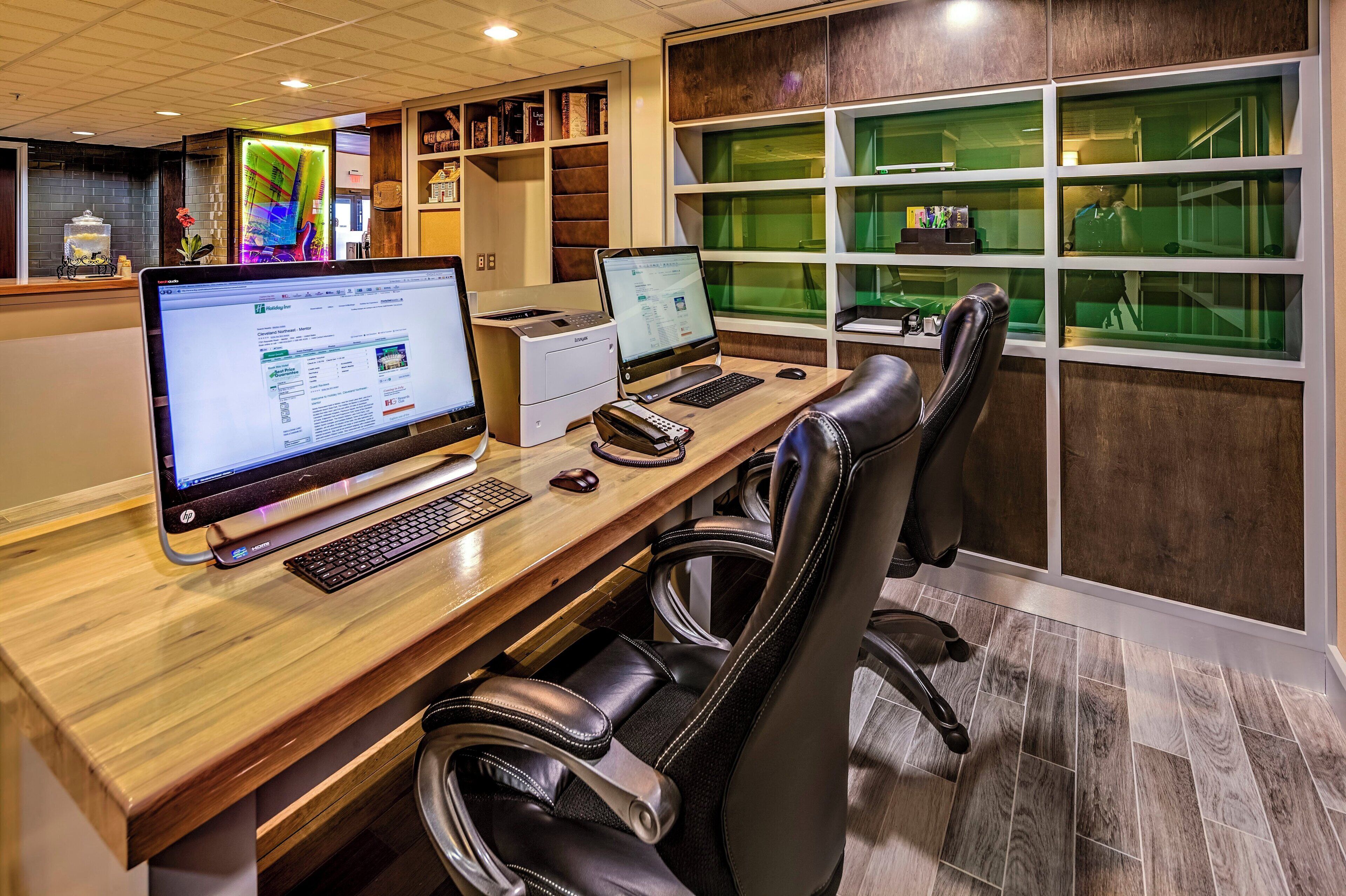 A modern office space with two desktop computers, a printer, and leather chairs.