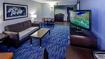 Quarto de hotel com sofá, mesa pequena, televisão e secretária com telefone.