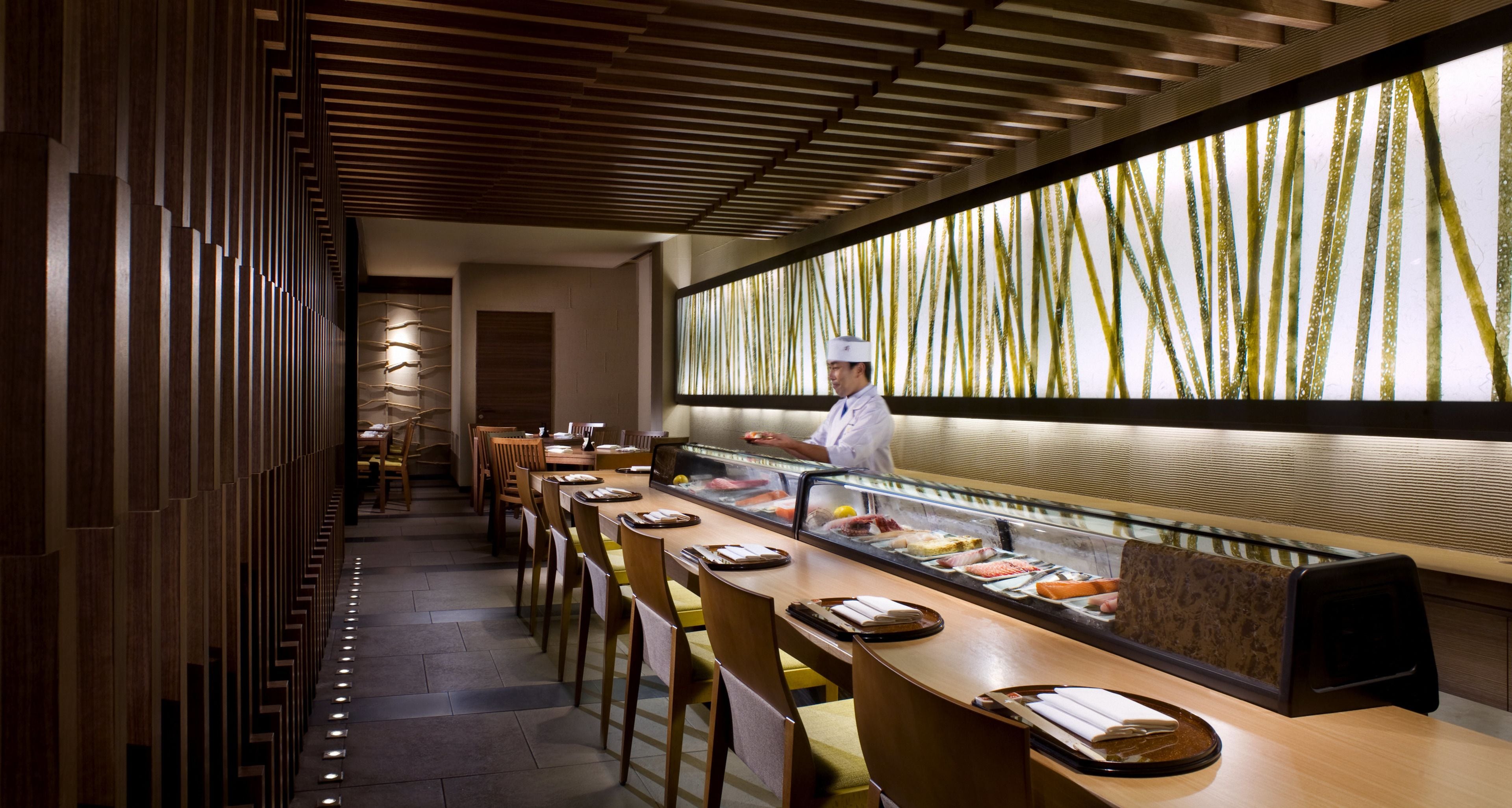 Un restaurant doté d’un bar à sushis, de lambris en bois et d’un chef qui prépare les plats.