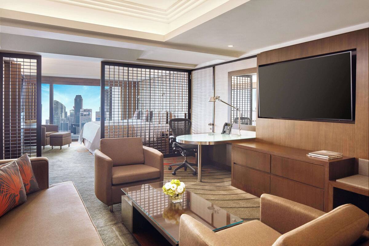 Una habitación de hotel moderna con vista a la ciudad, un televisor de pantalla plana grande, un escritorio con una silla y un sofá.