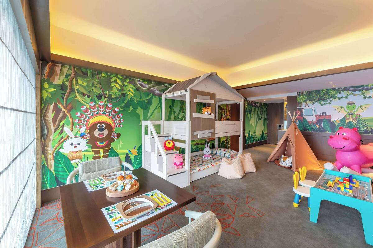 Un cuarto de juegos infantil con un mural con temática de jungla, una litera y una mesa de juegos llena de juguetes.