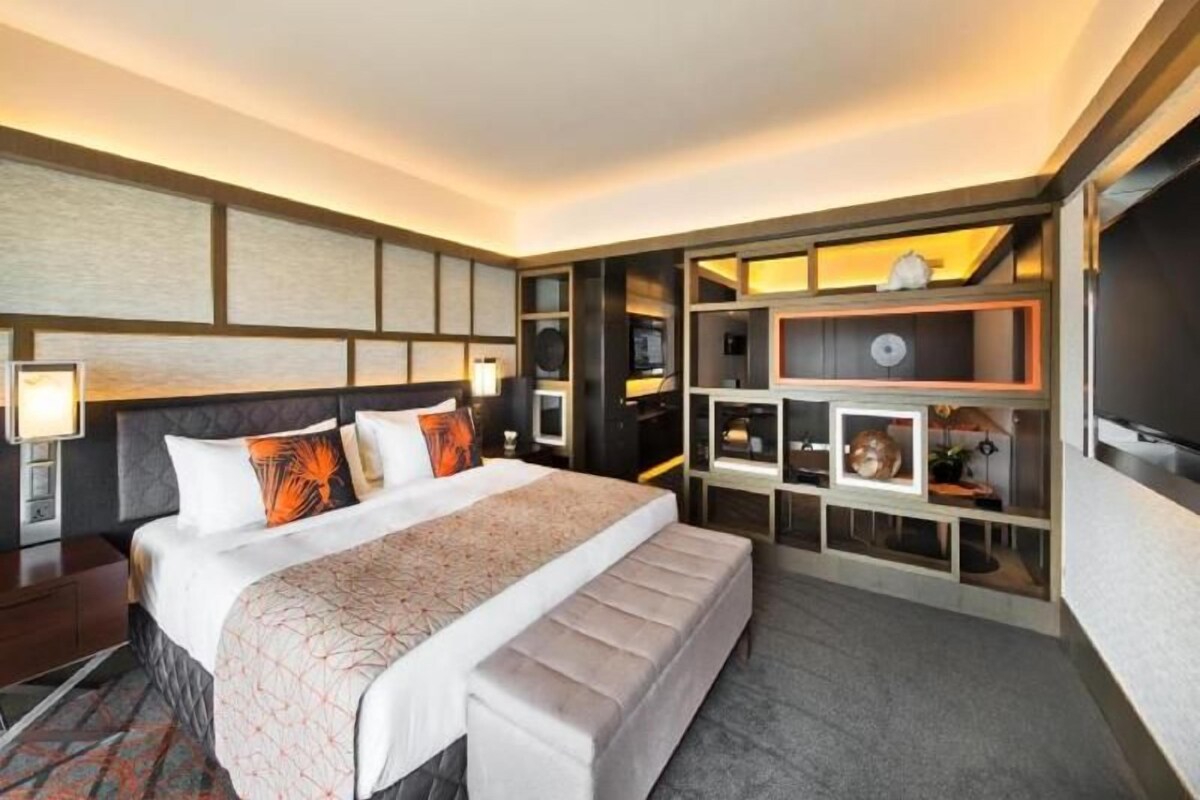 Een hotelkamer met een groot bed, een nachtkastje, een ingebouwde televisie en een opbergunit met planken.