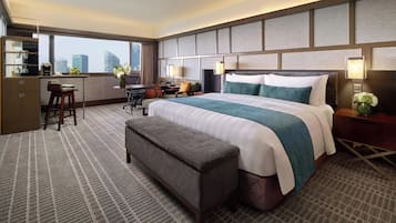 Habitación de hotel con una cama grande, un escritorio con una silla, un banco y vistas a la ciudad.