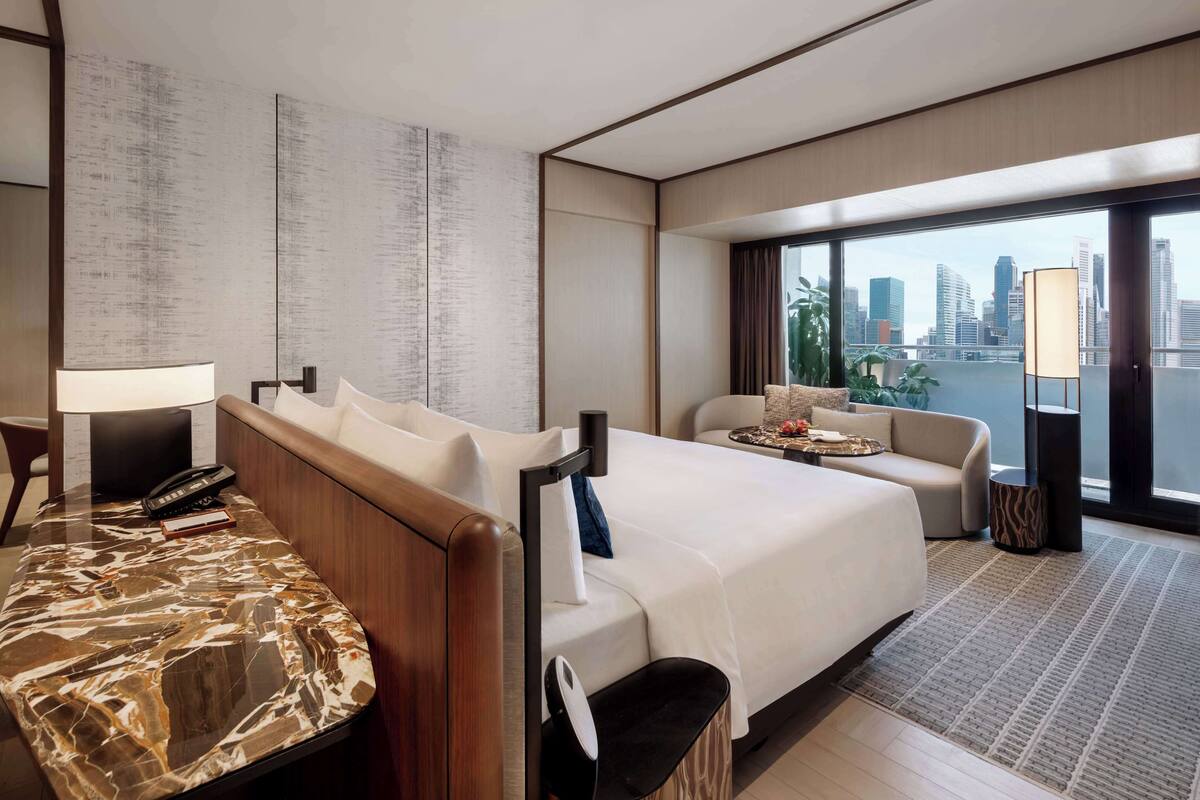 Una habitación de hotel moderna con una cama grande, un sofá, un escritorio con lámpara y vistas a la silueta urbana.