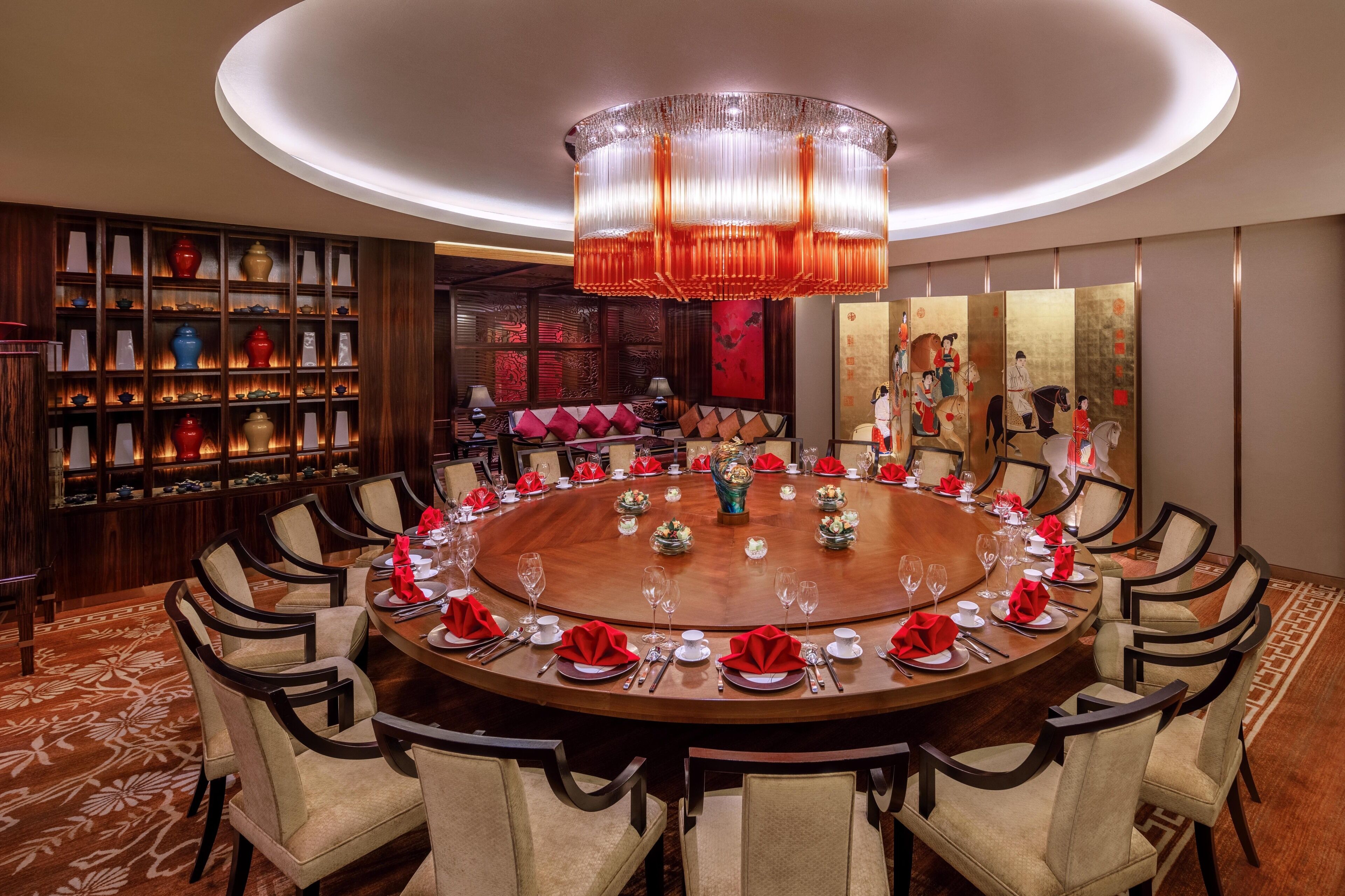 Una mesa redonda de comedor con sillas, una araña y una pared decorativa con jarrones.