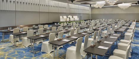 A conference room with rows of tables and chairs, a modern ceiling design, and chandeliers.