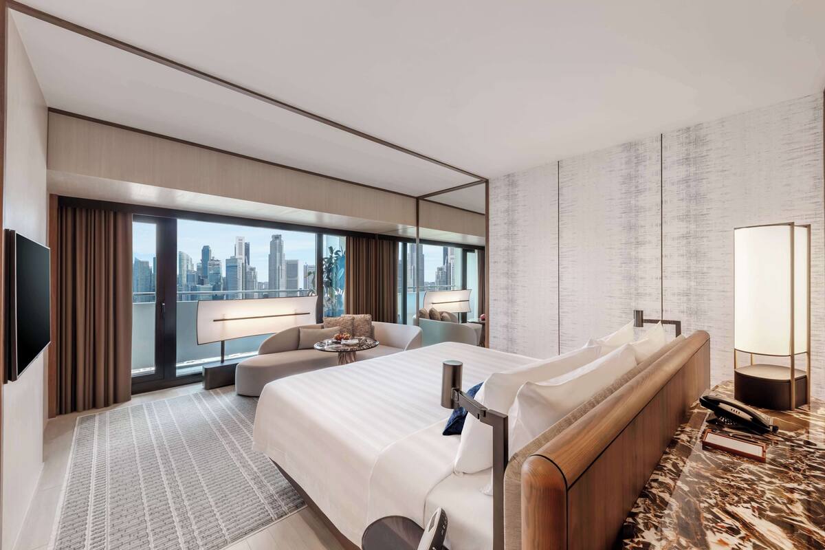Una habitación de hotel moderna con una cama grande, un sofá, un escritorio y vista a la ciudad.