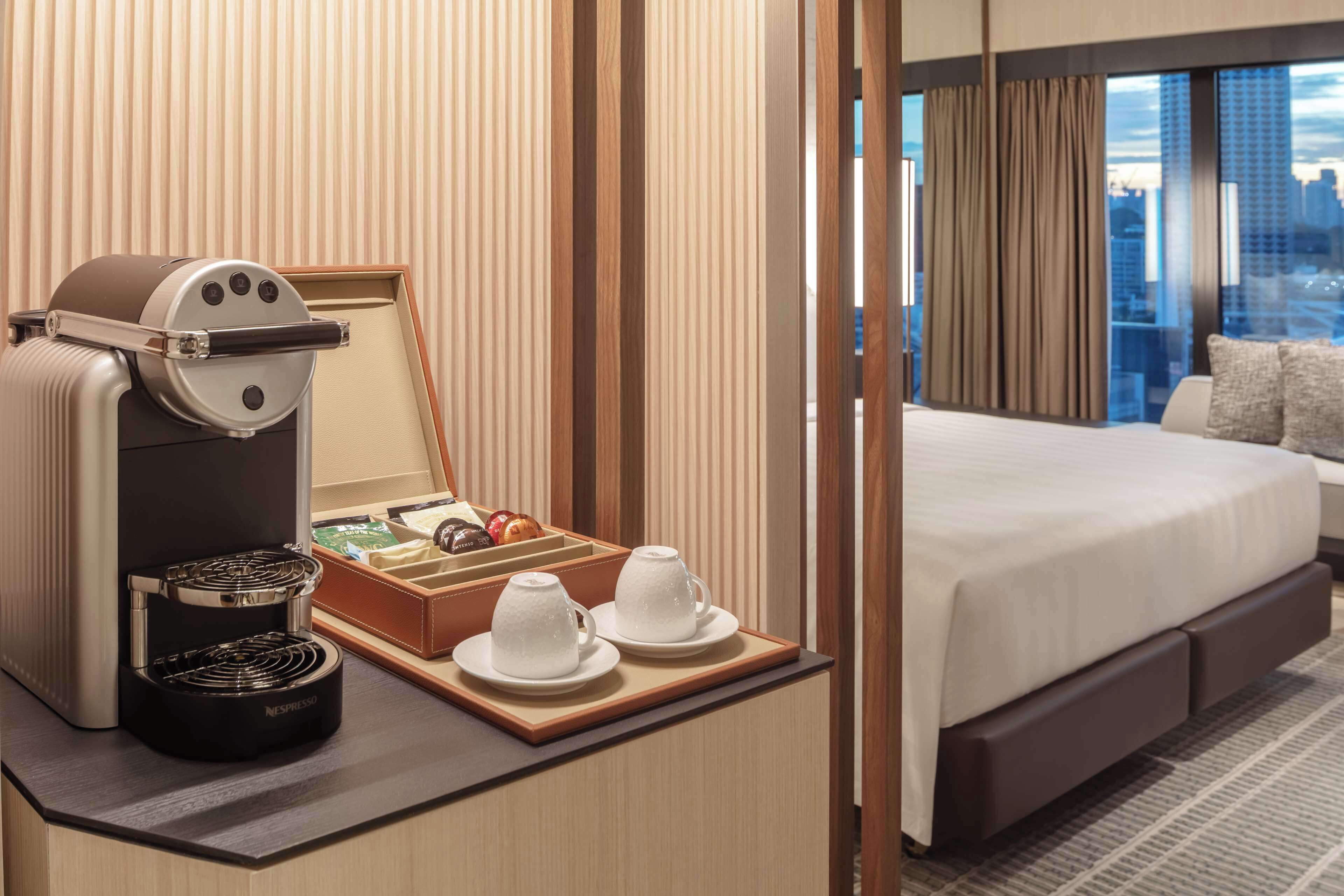 Una habitación de hotel con una cama, una cafetera y una bandeja con tazas y una caja de bombones.