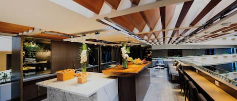 A modern kitchen with marble countertops, wooden beams, and a central island with fruit and flowers.