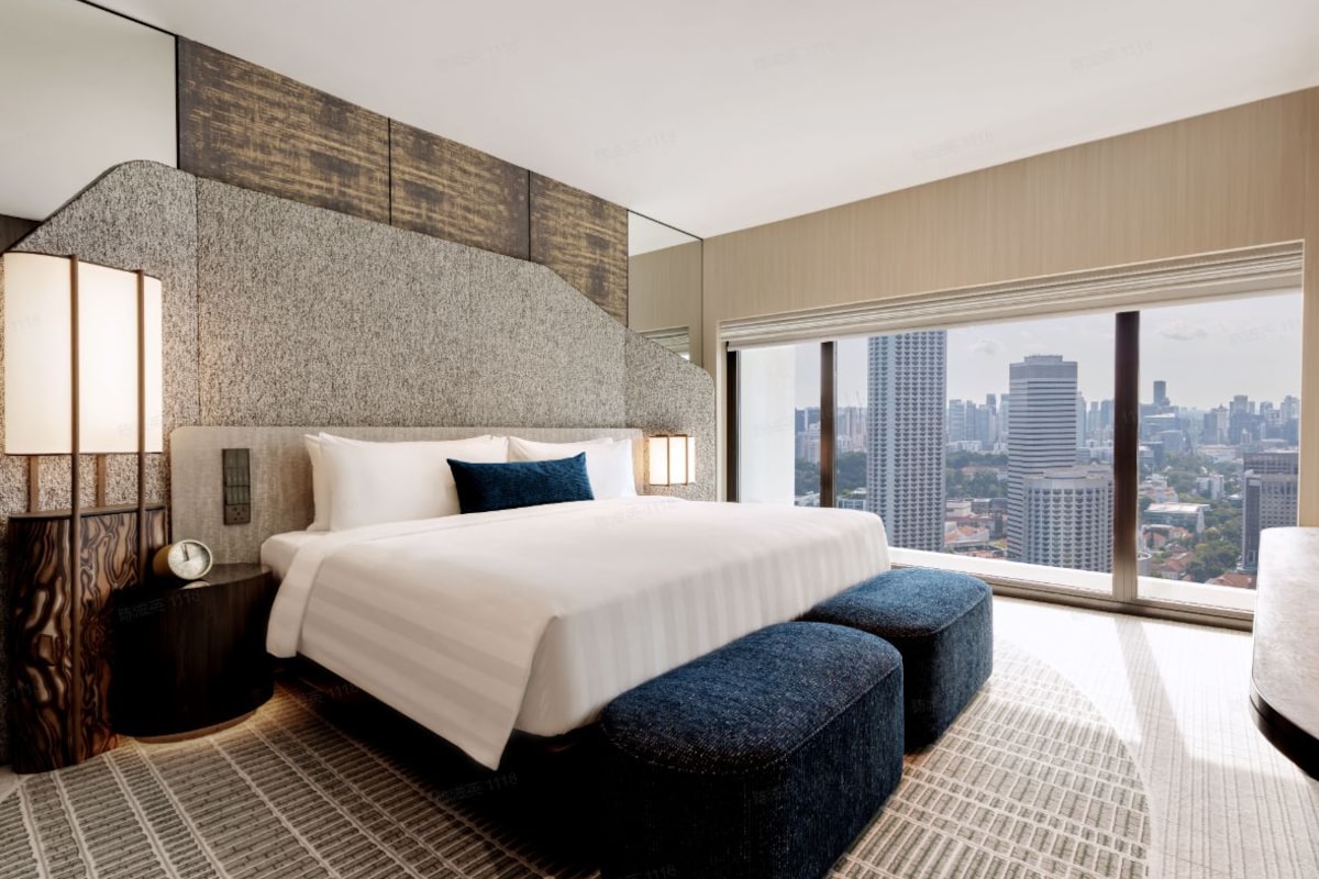 A modern hotel room with a large bed, a city view, and a unique textured wall.