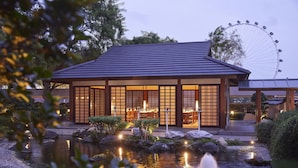 Un edificio de estilo japonés tradicional con un estanque de carpas y una fuente, rodeado de rocas y vegetación.
