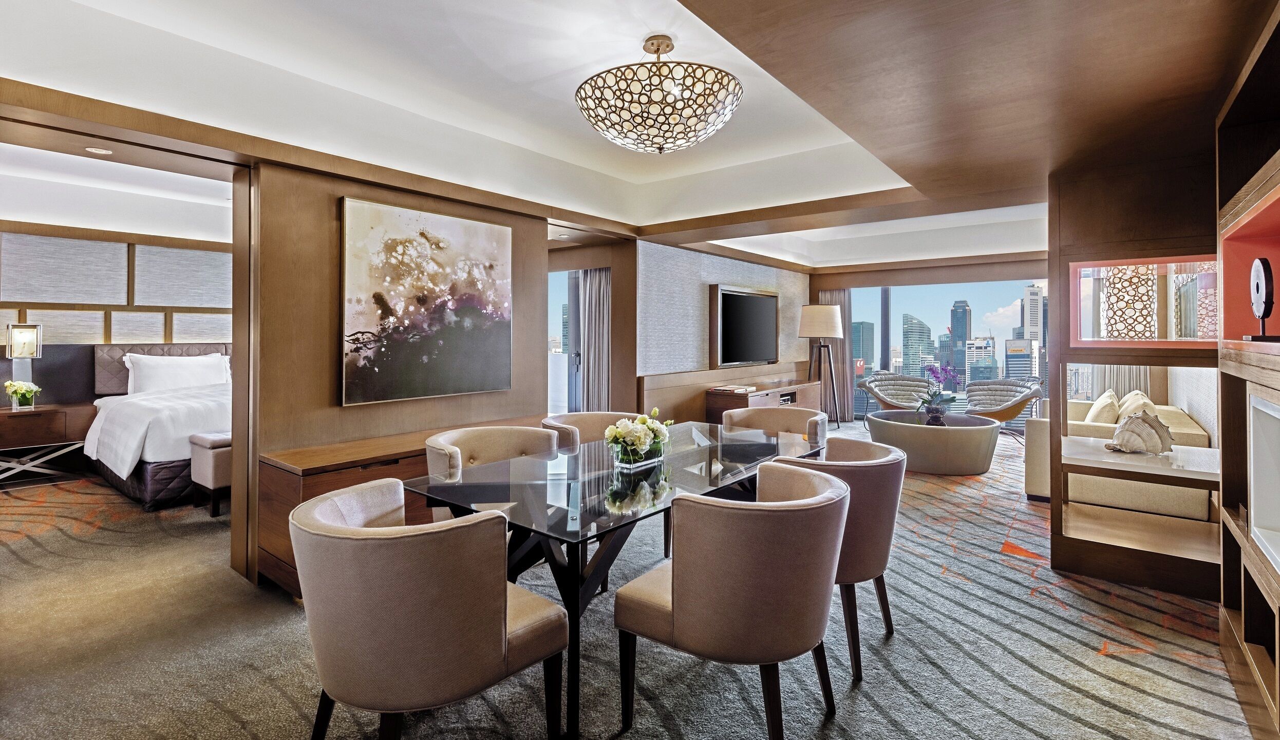 Habitación de hotel con comedor, un cuadro grande, televisor y vista a la ciudad.