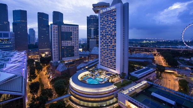 Un hotel de gran altura con un llamativo letrero Pan Pacific, rodeado de otros edificios altos y una noria al fondo.